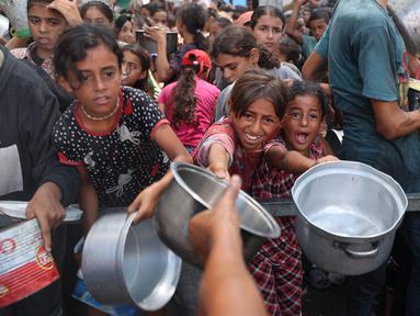 Anak-anak perempuan Palestina berkumpul untuk menerima makanan matang dari pusat distribusi makanan di kamp pengungsi Nuseirat di Jalur Gaza tengah pada 18 Agustus 2025. (Eyad BABA/AFP)
