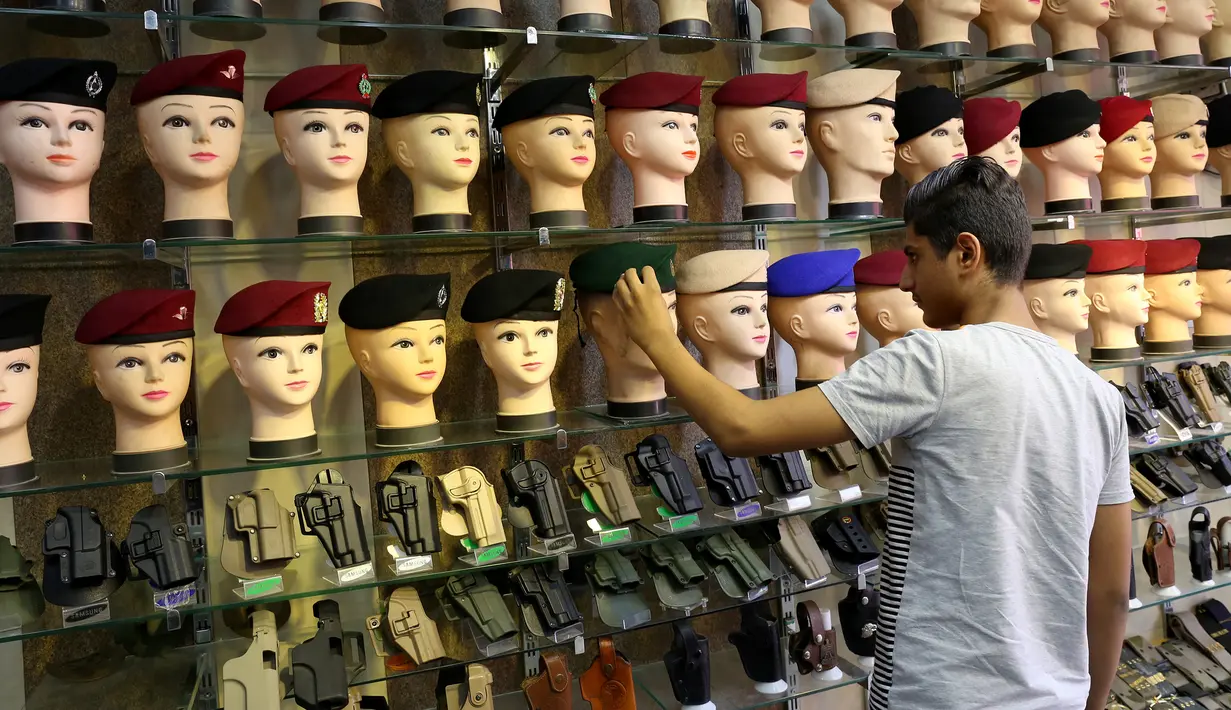 Seorang pria melihat baret militer dan pistol yang dipamerkan di jalan al-Khayyam di Baghdad (13/9). Perang yang berlangsung di Irak membuat para penjahit pakaian biasa kebanjiran orderan membuat seragam militer dan aksesorisnya. (AFP Photo/Sabah Arar)