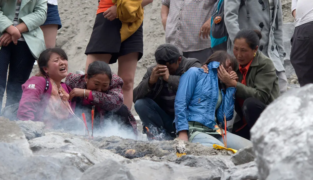 Keluarga korban menangis saat membakar dupa dan kertas ritual untuk menenangkan arwah orang yang tewas di lokasi tanah longsor di desa Xinmo, Sichuan, China (25/6). (AP Photo / Ng Han Guan)