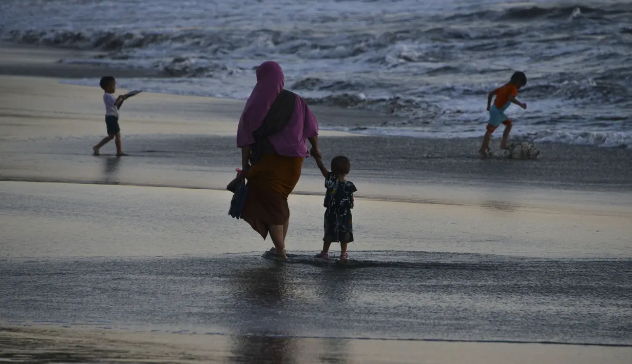 Seorang wanita bersama putranya berjalan di tepi pantai saat matahari terbenam di Banda Aceh pada 28 Juni 2019. Suasana eksotis menuju temaram bisa dinikmati sembari berjalan menyusuri pantai di tengah cahaya matahari yang mulai memerah. (Photo by CHAIDEER MAHYUDDIN / AFP)