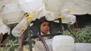 Seorang anak laki-laki Palestina berdiri di samping wadah plastik di atas troli, saat ia dan yang lainnya mengumpulkan air minum untuk keluarganya yang mengungsi dan tinggal di tempat penampungan setelah rumah-rumah mereka hancur akibat bombardir Israel, di kamp pengungsi Bureij, Jalur Gaza Tengah pada Senin 18 Mei 2026. (Eyad Baba/AFP)