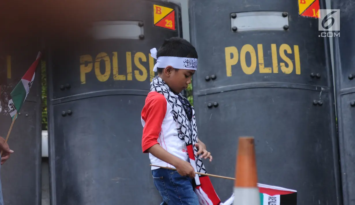 Seorang anak melintas di depan tameng polisi saat aksi dukungan bagi negara Palestina di depan Kedubes AS, Jakarta, Minggu (10/12). Mereka memprotes keputusan Presiden Trump yang mengakui Yerusalem jadi Ibu Kota Israel. (Liputan6.com/Helmi Fithriansyah)