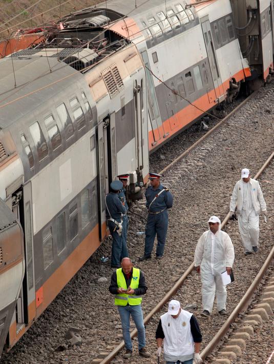 Aparat kepolisian berdiri dekat sebuah kereta api yang keluar jalur dan terguling di Sidi Bouknadel, Maroko, Selasa (16/10). Masinis kereta api dipastikan menjadi salah satu korban tewas dalam kecelakaan tersebut. (AP/Abdeljalil Bounhar)