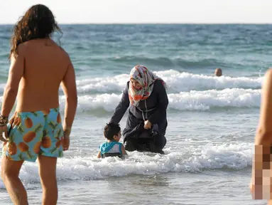 Seorang wanita Muslim bersama anaknya saat berada di pantai di Tel Aviv, Israel pada 22 Agustus 2016. Meski berada di pantai, wanita muslim ini tetap mengenakan jilbab dan busananya. (REUTERS / Baz Ratner)
