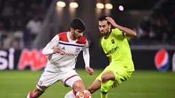 Gelandang Lyon, Martin Terrier melewati Sergio Busquets pada leg 1, babak 16 besar Liga Champions yang berlangsung di stadion Parc Olympique Lyonnais, Lyon, Rabu (20/2). Barcelona bermain imbang 0-0 kontra Lyon. (AFP/Franck Fife)