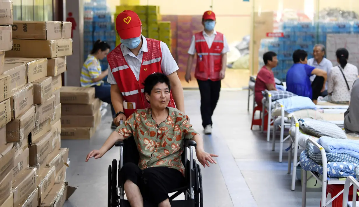 Sukarelawan mendorong kursi roda penduduk desa di tempat pengungsian sementara Sekolah Menengah No.168, Hefei, Provinsi Anhui, China, Rabu (29/7/2020). Makanan gratis, konseling psikologis, dan bantuan kehidupan sehari-hari disediakan di tempat pengungsian sementara tersebut. (Xinhua/Liu Junxi)