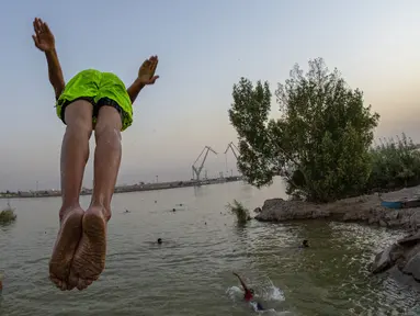 Seorang pemuda terjun ke Sungai Shatt Al-Arab di Kota Basra, Irak, Selasa (9/6/2020). Sungai yang memiliki panjang sekitar 200 Km ini menandai perbatasan antara Irak dan Iran. (Hussein FALEH/AFP)
