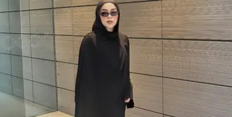 Sivia mengenakan pashimina hitam panjang polos serasi dengan abaya hitam polosnya. Dipadukan kacamata hitam sambi membawa tas hitamnya. Mengenakan sepatu sneakers hijau. [@siviazizah]