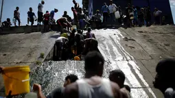 Orang-orang mengumpulkan air yang keluar melalui saluran pembuangan air limbah yang mengalir ke Sungai Guaire di Caracas, 11 Maret 2019. Pemadaman listrik selama berhari-hari di Venezuela berdampak terhadap krisis air. (REUTERS/Carlos Garcia Rawlins)