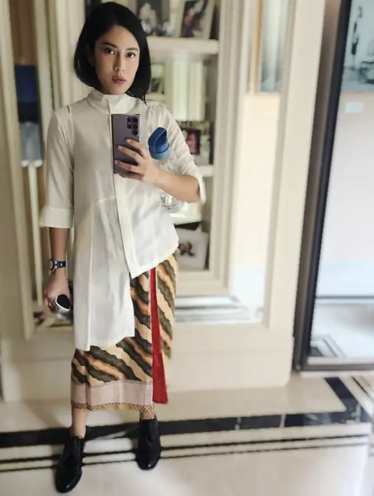 Tampilan  Dian Sastrowardoyo mengenakan kemeja panjang putih dan bawahan kain lilit bisa dipadukan dengan sepatu loafers hitam. Cocok untuk tampil stylish di Hari Raya. Credit: Instagram (@therealdisastr)