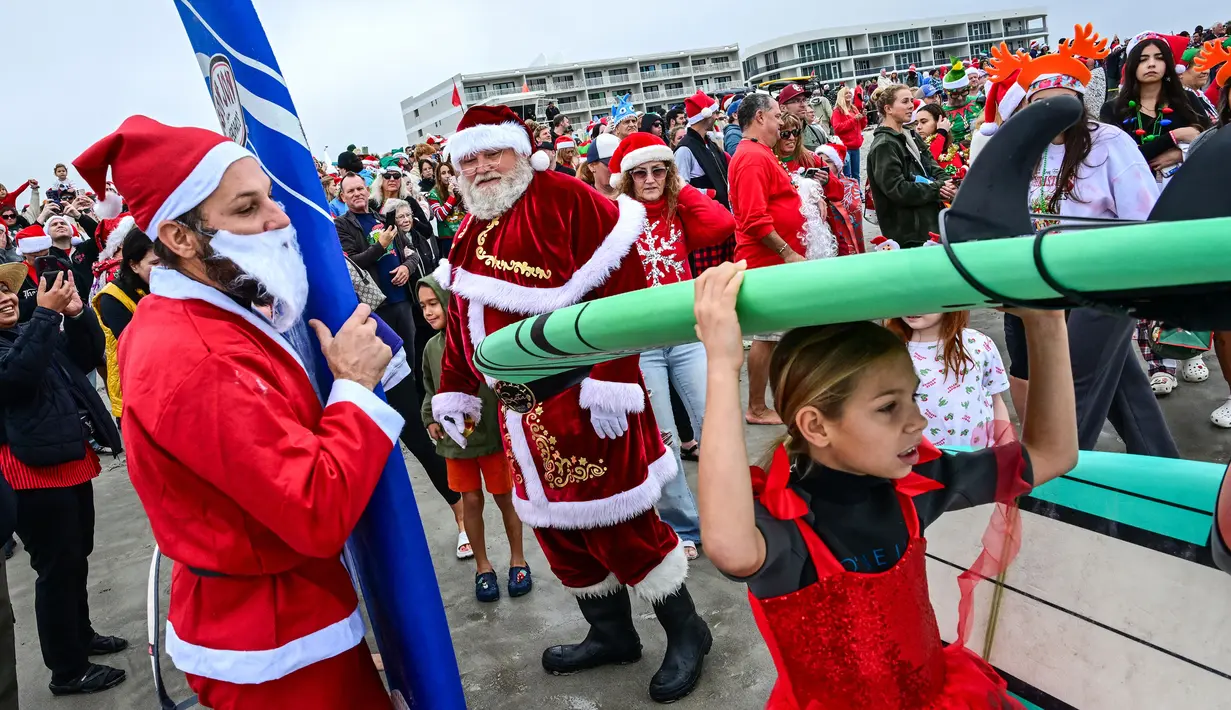 Sejumlah pengunjung berkostum Sinterklas bersiap melakukan selancar dalam acara Surfing Santa yang berlangsung di Pantai Cocoa, Florida, Amerika Serikat, Selasa (24/12/2024) waktu setempat. (AFP/Giorgio Viera)