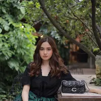 Syifa Hadju duduk di sebuah bangku taman dengan menampilkan Tabby Shoulder Bag 20 Coach (Foto Dok: KANMO GROUP).