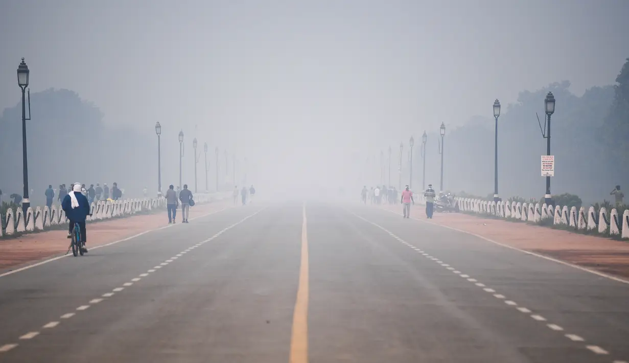 Orang-orang melintas di sepanjang jalan Rajpath dekat Gerbang India di tengah kondisi asap tebal yang menyelimuti sehari setelah perayaan Diwali, festival cahaya Hindu, di New Delhi pada Minggu (15/11/2020). (Photo by Sajjad HUSSAIN / AFP)