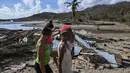 Warga berjalan di tengah puing-puing rumah yang rusak akibat Badai Melissa di desa Boca de Dos Rios, provinsi Santiago de Cuba, Kuba pada Kamis 30 Oktober 2025. Pihak berwenang Kuba juga mengevakuasi lebih dari 735.000 orang dari daerah rawan sebelum badai tiba. (YAMIL LAGE/AFP)