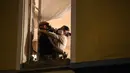 Pria yang mengenakan masker gas merangkul wanita yang mengenakan masker saringan udara di jendela tempat tinggal mereka di Kota Nice, Riviera, Prancis, 24 Maret 2020. Organisasi Kesehatan Dunia (WHO) mengumumkan virus corona COVID-19 sebagai pandemi sejak 11 Maret 2020 lalu. (VALERY HACHE/AFP)