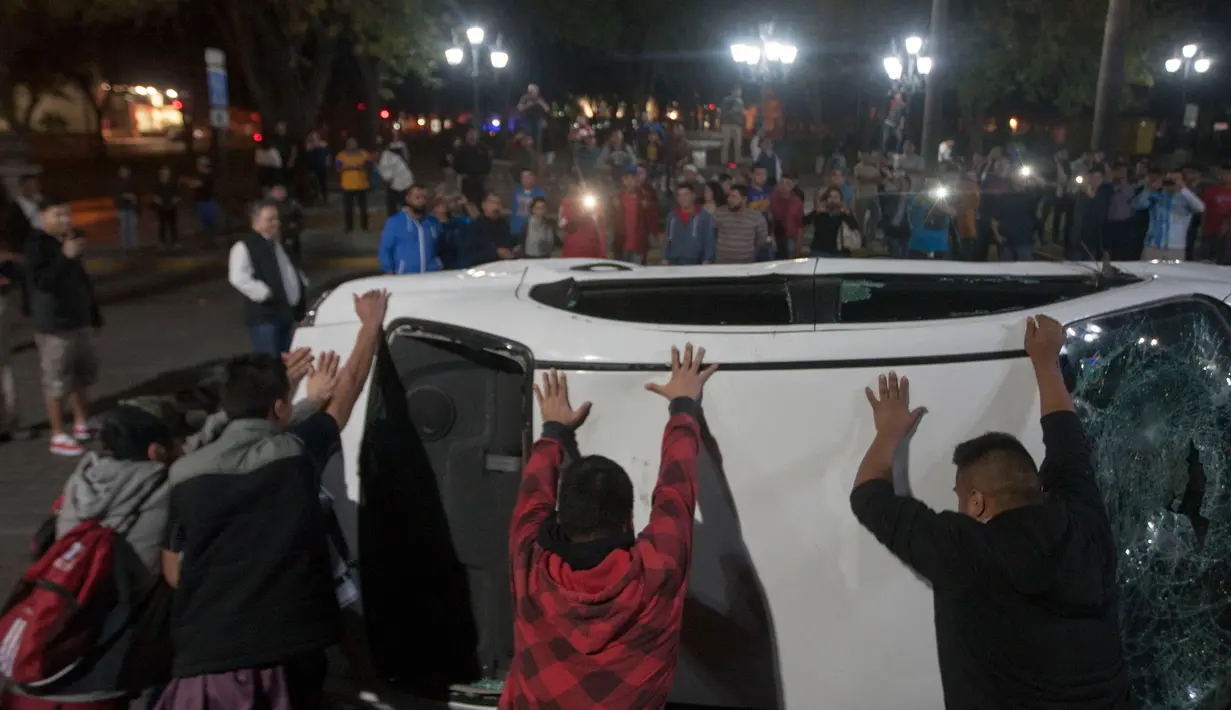 Massa berusaha membalikkan mobil milik stasiun TV dalam unjuk rasa kenaikan harga BBM hingga 20% di Monterrey, Meksiko, Kamis (5/1). Hal ini seiring dengan berakhirnya subsidi bahan bakar di negara kawasan Amerika Selatan ini. (Julio Cesar Aguilar/AFP)
