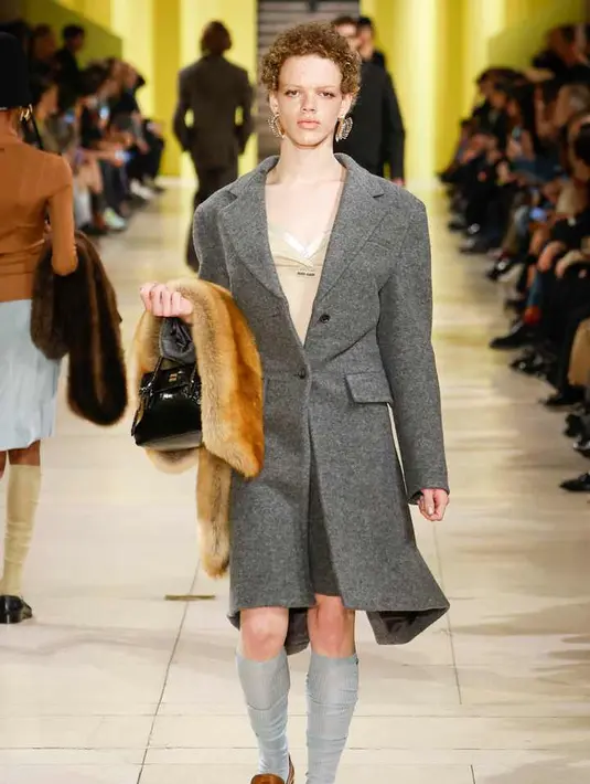 Miu Miu dikenal sebagai “adik ceria” dari Prada yang lebih akademis dan serius. Koleksi ini membawa nuansa muda dengan siluet remaja yang diperbarui, seperti celana track pleated, setelan rok wol, dan bolero terstruktur. Detail asimetris pada pullover ber-resleting dan gaun floral yang jatuh dari bahu menciptakan kesan “meminjam pakaian kakak” yang sedikit kebesaran. [Dok/Miu Miu].