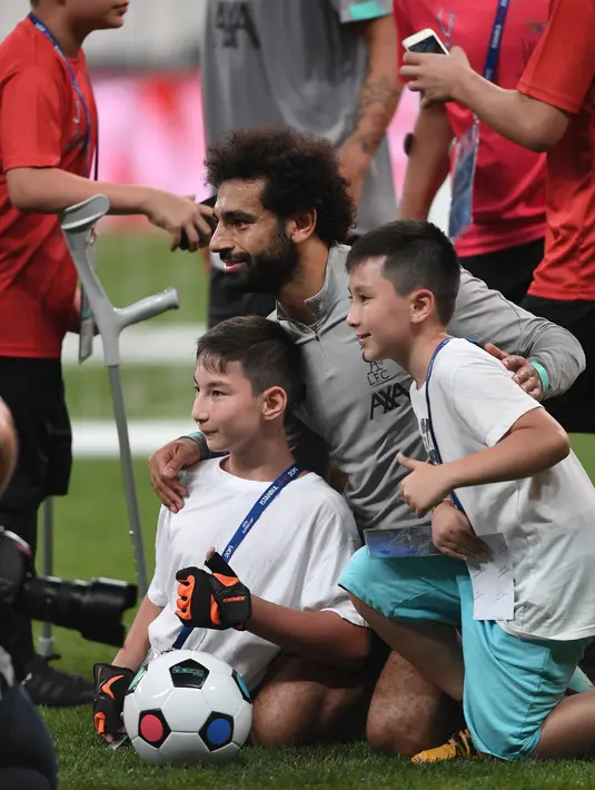 Gelandang Liverpool, Mohamed Salah foto bersama seorang anak tanpa memiliki kaki usai bermain selama sesi latihan jelang bertanding melawan Chelsea pada Piala Super Eropa 2019 di Stadion Taman Besiktas, di Istanbul (13/8/2019). (AP Photo/Lefteris Pitarakis)