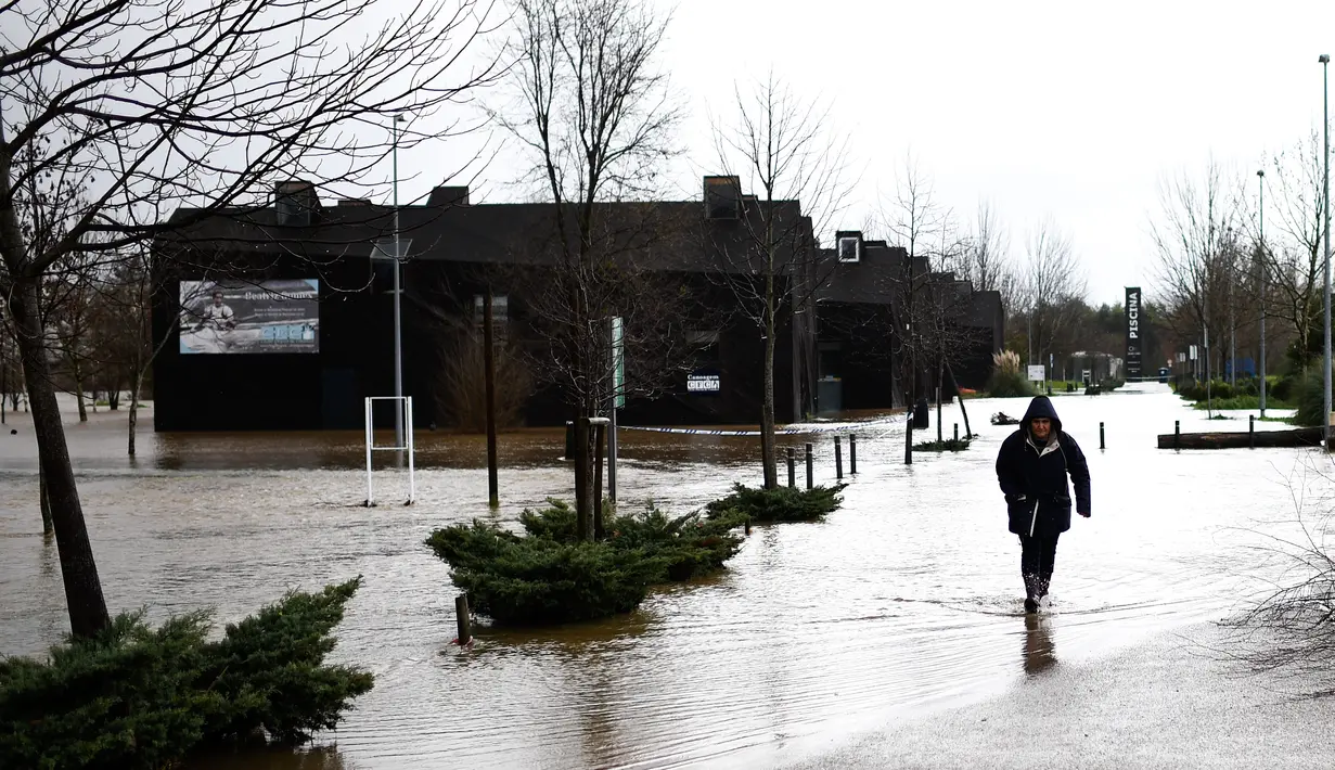 Seorang wanita melalui genangan air di Coimbra, Portugal (14/2/2016). Banjir yang terjadi di Coimbra diakibatkan oleh meluapnya sungai Mondego setelah diguyur hujan selama 24 jam. (AFP Photo /Francisco Leong)