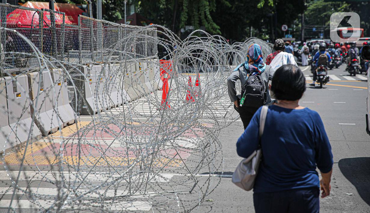 Warga berjalan dekat kawat berduri di kawasan Jalan MH Thamrin, Jakarta, Kamis (2/12/2021). Polda Metro Jaya memasang barikade di sejumlah titik menuju kawasan Patung Kuda-Monumen Nasional (Monas) Jakarta Pusat guna mengantisipasi kerumunan massa aksi Reuni 212. (Liputan6.com/Faizal Fanani)