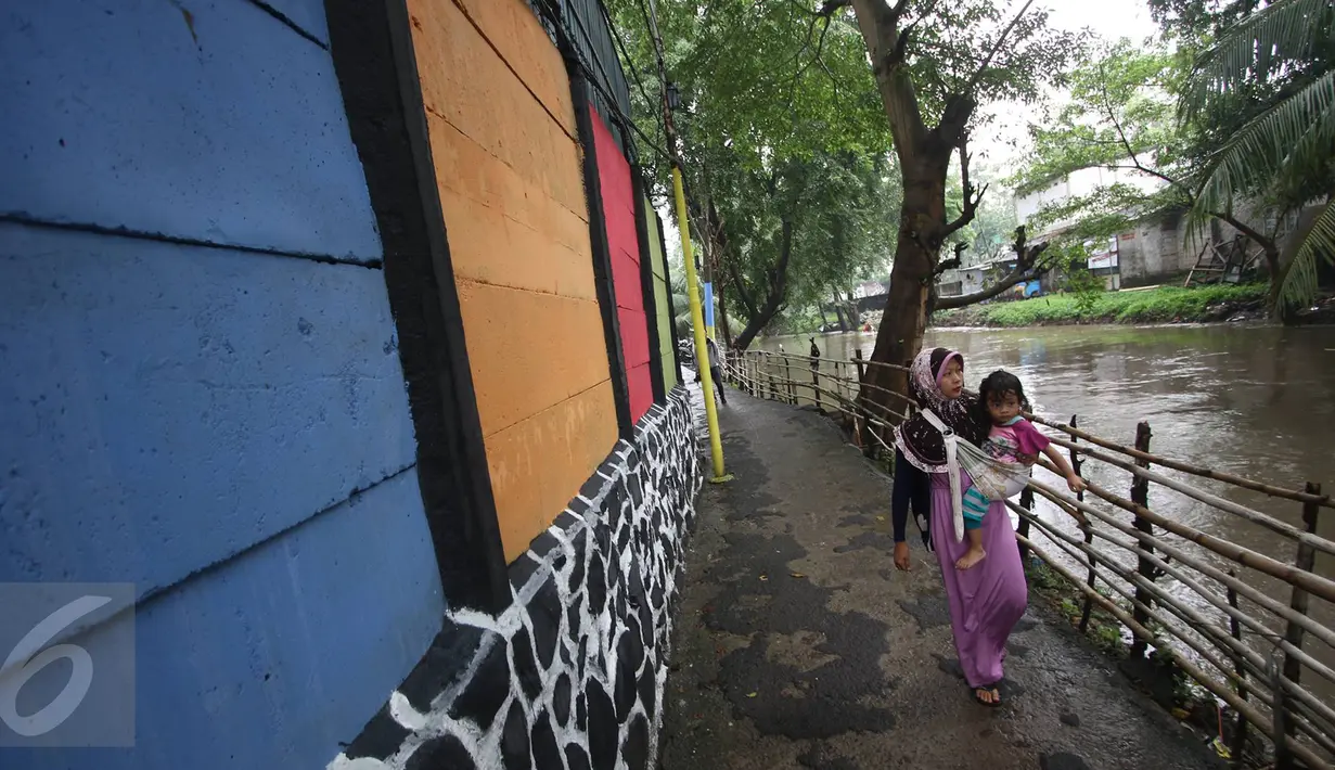 Warga melintas dekat tembok warna-warni di Kampung Penas Tanggul, Cipinang Besar Selatan, Jakarta, Kamis (23/3). Kampung warna-warni tanpa rokok itu dibuat warga sebagai bentuk upaya perlindungan bagi perempuan dan anak. (Liputan6.com/Immanuel Antonius)