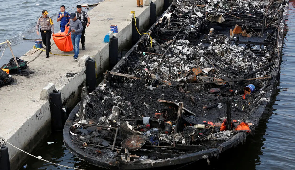 Petugas kepolisian bersama Tim SAR gabungan mengevakuasi kantong jenazah berisi penumpang kapal Zahro Express yang terbakar, di Pelabuhan Muara Angke, Minggu (1/1). Kapal penumpang tersebut terlihat dalam kondisi gosong. (REUTERS/Darren Whiteside)