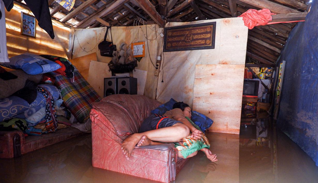 Seorang warga beristirahat di sofa di rumahnya yang terendam banjir di desa Sukajaya di Serang (1/3/2022).  Banjir merendam Kota Serang akibat hujan deras yang turun sejak Senin malam (28/2/2022) hingga hari ini. (AFP/Dziki Oktomauliyadi)