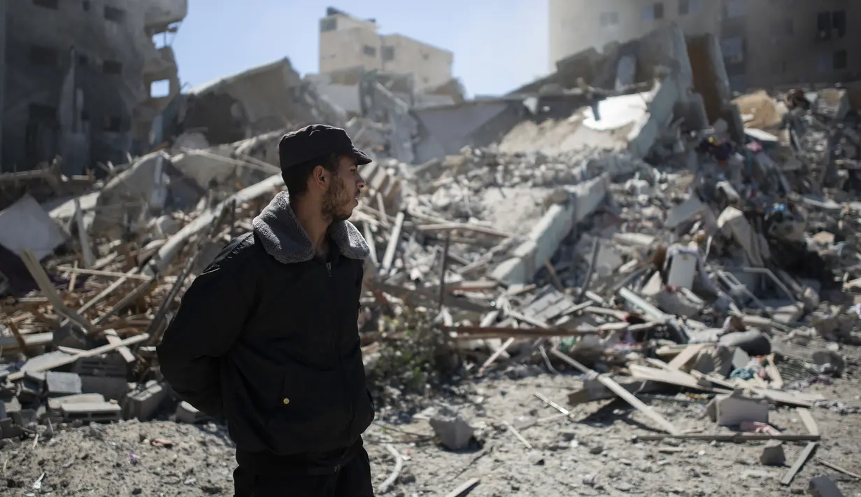 Polisi Palestina berdiri dekat reruntuhan bangunan kantor The Associated Press yang hancur akibat serangan udara Israel di Kota Gaza, Sabtu, 15 Mei 2021. Gedung tersebut juga menampung Al Jazeera dan sejumlah kantor serta apartemen. (AP Photo/Khalil Hamra)
