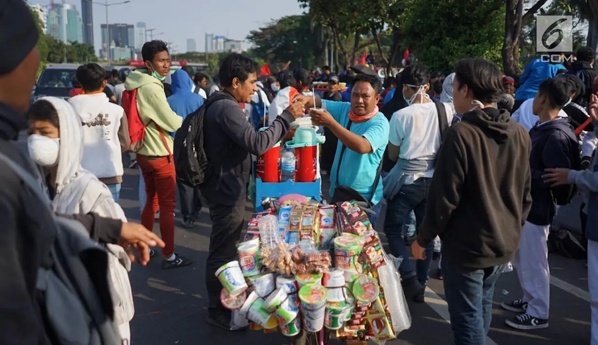 Pedagang melayani pembeli minuman saat berjualan di antara massa aksi di jalan tol dalam kota yang berada di depan Gedung DPR RI, Jakarta, Senin (30/9/2019). Adanya aksi unjuk rasa di sekitar lokasi dimanfaatkan para pedagang asongan untuk mencari rezeki. (Liputan6.com/Immanuel Antonius)