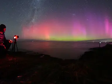 Seorang pria memotret Aurora Australis saat bersinar di cakrawala di atas perairan Danau Ellesmere di pinggiran Christchurch, Selandia Baru pada 24 April 2023. (AFP/Sanka Vidanagama)
