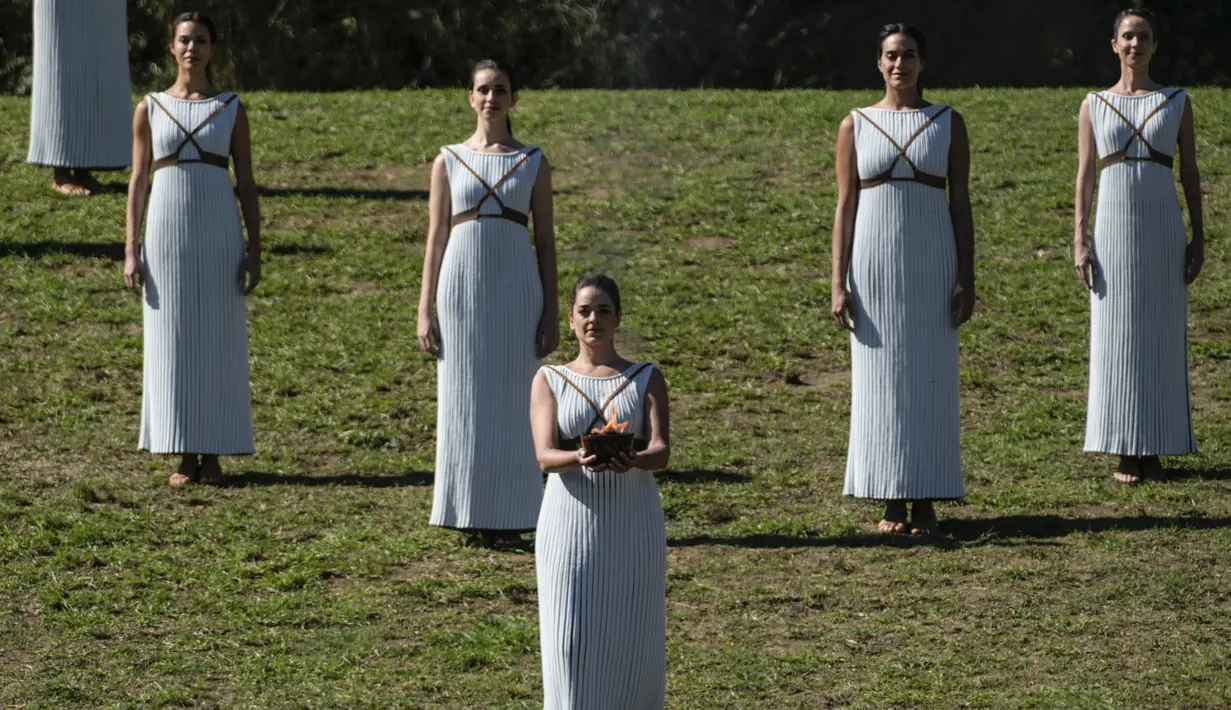 Aktris Yunani Xanthi Georgiou yang berperan sebagai High Priestess berjalan dengan api ke pembawa obor pertama pembalap ski alpine Yunani Ioannis Antoniou saat penyalaan api Olimpiade di situs Olympia, Yunani, Senin (18/10/2021). (AP Photo/Petros Giannakouris)