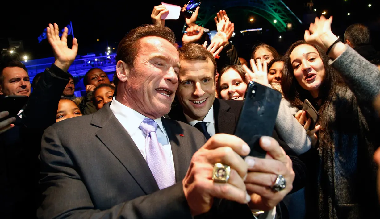 Aktor yang juga mantan Gubernur California, Arnold Schwarzenegger berswafoto dengan Presiden Prancis, Emmanuel Macron (tengah) berlatar belakang Menara Eiffel seusai menghadiri KTT One Planet Summit di Paris, Selasa (12/12). (AP/Thibault Camus, Pool)