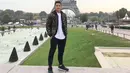 <p>Tampak berpose dengan latar Menara Eiffel, Jonatan Christie mengenakan t-shirt putih, yang ditumpuknya dengan puffer hoodie jacket bermotif army, jogger pants hitam, dan sneakers hitam. Foto: Instagram.</p>