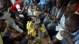 Sejumlah pria menggunakan selang kecil meminum air beralkohol dari pot yang disebut Busaa di daerah Nairobi, Kenya, Rabu (8/11). (AFP Photo/Simon Maina)