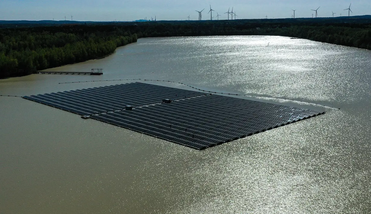 <p>Pemandangan dari udara menunjukkan panel surya dengan turbin angin di kejauhan di pabrik fotovoltaik terapung di danau Silbersee di Haltern, Jerman barat (22/4/2022). Taman surya terapung terbesar di Jerman saat ini sedang dibangun. (AFP/Ina Fassbender)</p>