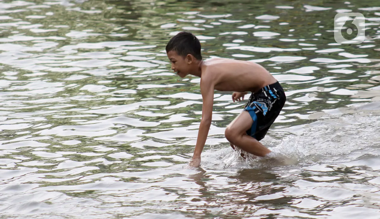 Seorang anak bermain di genangan air akibat banjir rob di kawasan pintu masuk Pelabuhan Nizam Zachman, Muara Baru, Jakarta, Jumat (5/6/2020). Banjir rob di Pelabuhan Muara Baru tersebut terjadi akibat cuaca ekstrem serta pasang air laut. (Liputan6.com/Helmi Fithriansyah)
