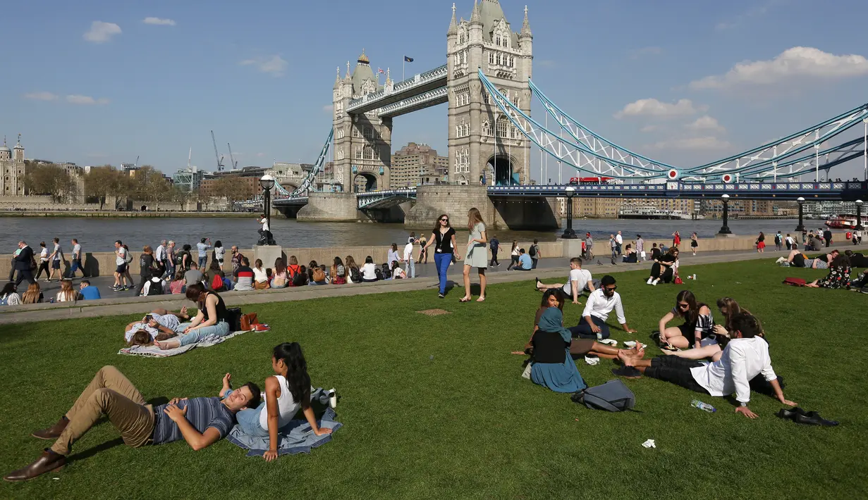 Orang-orang bersantai di tepi Sungai Thames dan Tower Bridge di London, Inggris, Jumat (20/4). Selain bermain di sungai, masyarakat Inggris juga biasa mengisi musim semi dengan berjemur di taman. (Daniel LEAL-OLIVAS/AFP)