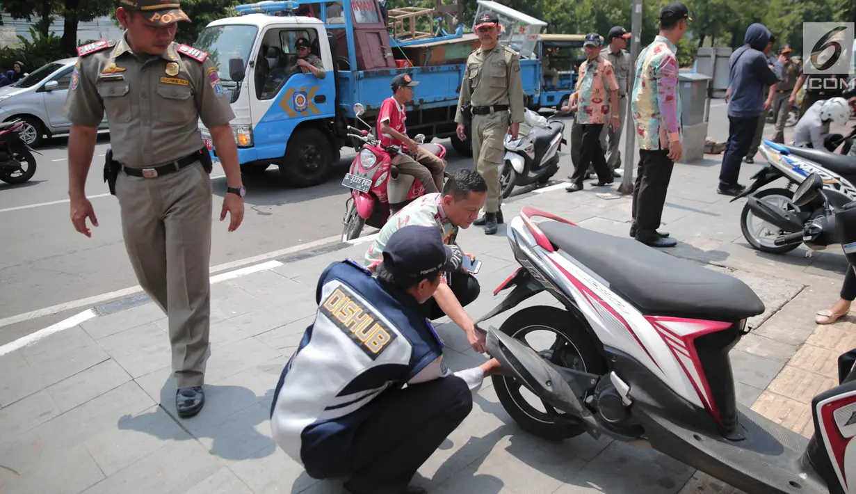 Petugas Dishub DKI menggembosi ban sepeda motor yang nekat parkir liar di trotoar sepanjang Jalan Kramat Raya, Senen, Jakarta, Jumat (22/9). Razia dilakukan untuk mengembalikan fungsi trotoar sebagai jalur pedestrian. (Liputan6.com/Faizal Fanani)