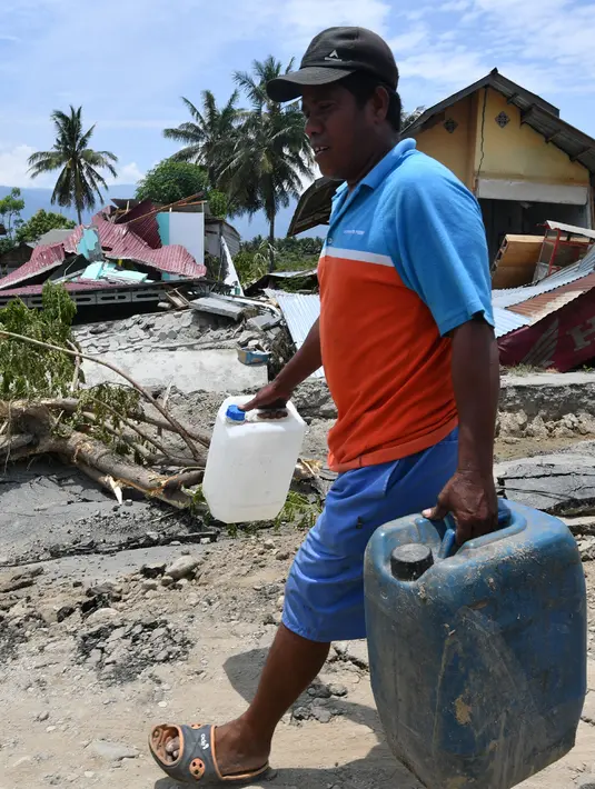 Seorang pria membawa jeriken melewati rusak usai gempa dan tsunami melanda Kabupaten Sigi, Sulawesi Tengah, Kamis (4/10). BNPB mengerahkan helikopter untuk mengatasi pengiriman bantuan ke sejumlah tempat yang terisolir di Sigi. (ADEK BERRY/AFP)