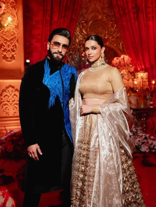 Deepika Padukone tampil menawan berpose bersama sang suami. Ia memilih sari bernuansa emas yang mewah, ditambah aksesori yang menyempurnakan keseluruhan penampilannya. [Foto: Instagram/asianweddingmag]
