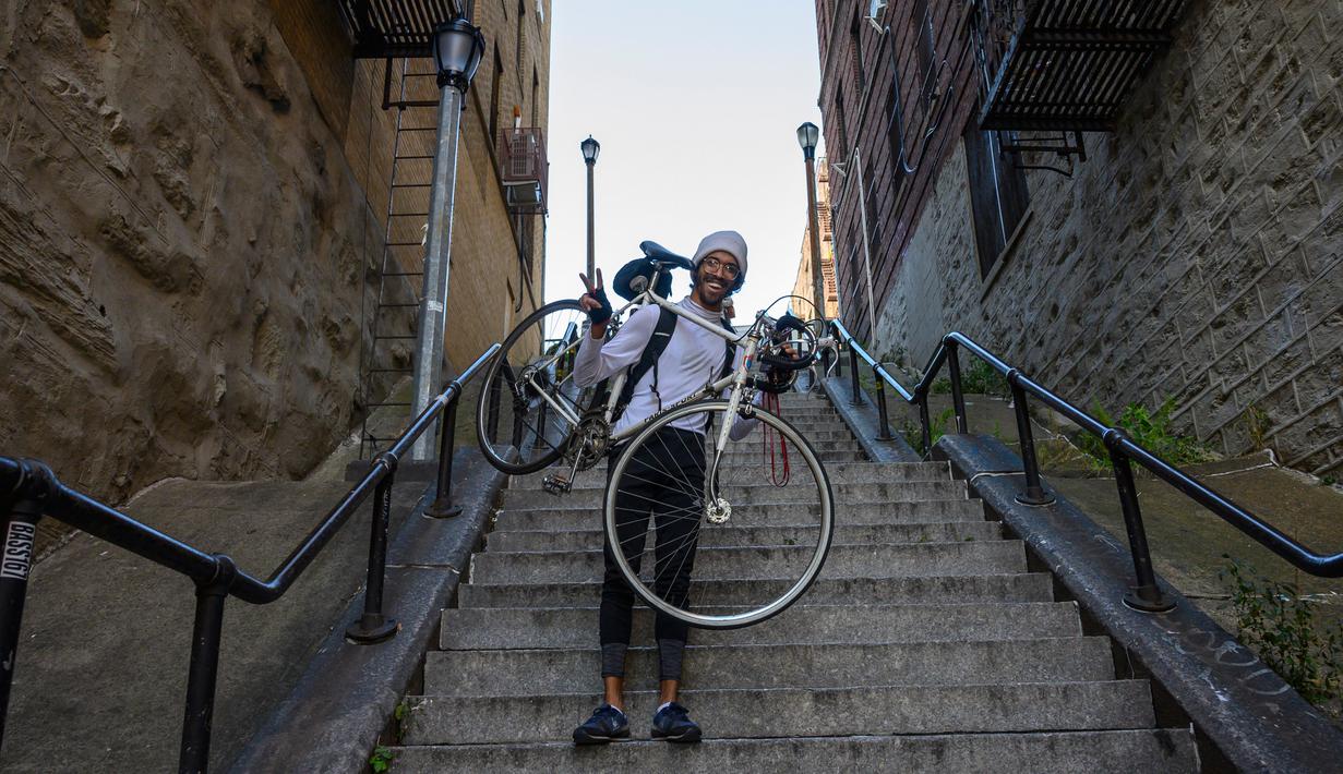 Elliott Raylassi, seorang penduduk lokal sejak tahun 2001, membawa sepedanya menaiki tangga di kawasan Bronx, New York, 23 Oktober 2019. Wisatawan memadati tangga panjang itu untuk berpose ala Joker atau sekadar mengunggahnya di Instagram. (Don Emmert / AFP)