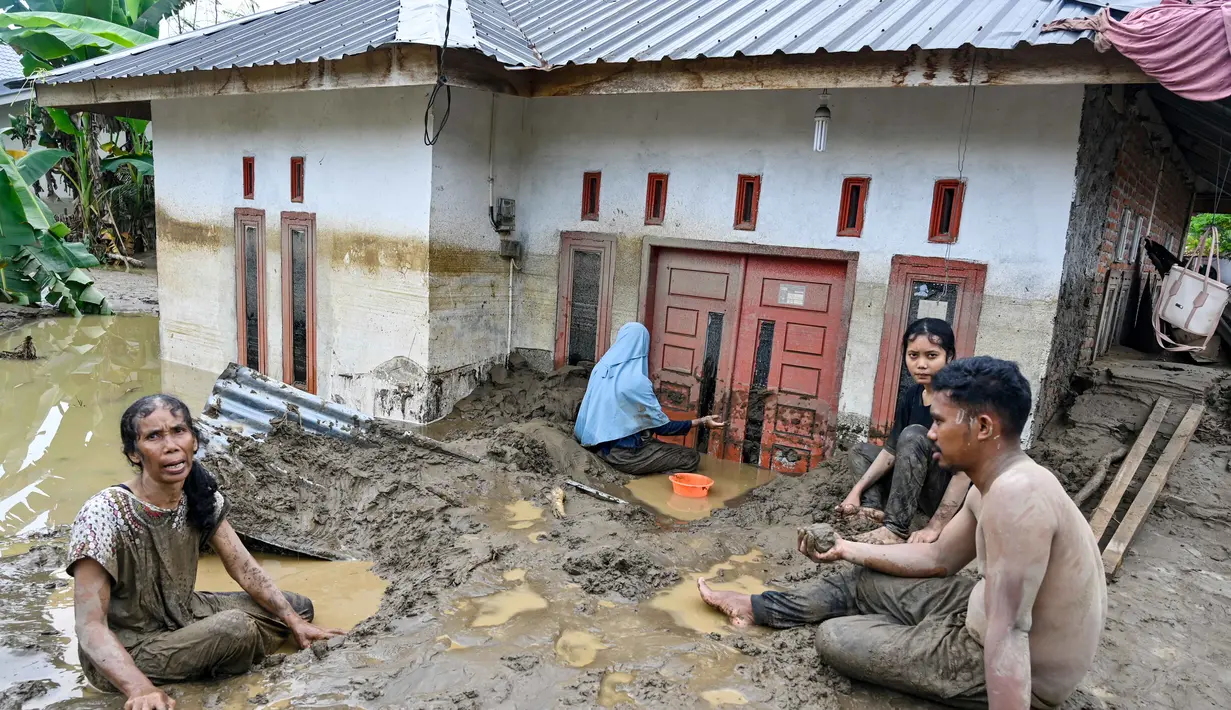 Air luapan sungai menerjang pemukiman warga dan memutus akses transportasi. Tampak dalam foto, warga membersihkan lumpur tebal dari pintu masuk rumah yang terendam banjir bandang di Meureudu, Kabupaten Pidie Jaya, Provinsi Aceh, Jumat 28 November 2025. (CHAIDEER MAHYUDDIN/AFP)