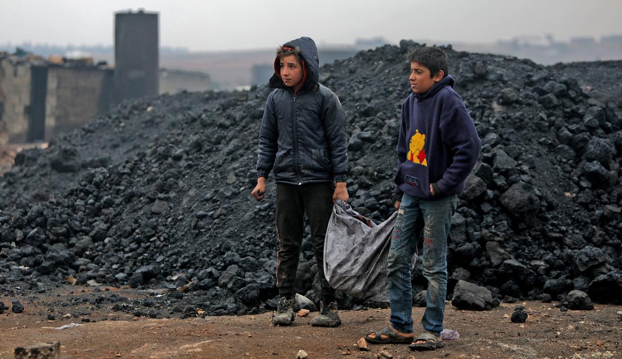 Dua anak Suriah mengangkut batu bara saat mereka bekerja di kilang minyak darurat dekat Kota al-Bab yang dikuasai Turki, Suriah, 20 November 2021. Sebanyak 1,6 juta anak Suriah juga berisiko putus sekolah. (Bakr ALKASEM/AFP)