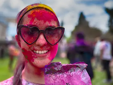 Seorang wanita yang mengenakan kacamata hitam memoles wajahnya dengan bedak warna-warni saat merayakan Holi, festival warna Hindu, di bagian Encino, Los Angeles, Minggu, 24 Maret 2024. (AP Photo/Richard Vogel)