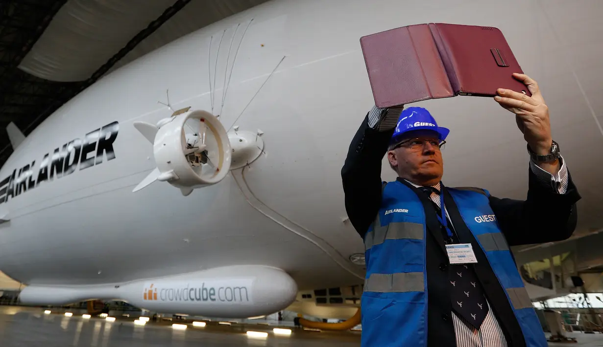 Seorang pria berselfie dengan latar belakang Airlander 10 saat peluncuran media di Cardington Airfield, Bedfordshire, Senin (21/3). Pesawat dengan panjang 90 meter ini mempunyai lambung besar yang bisa dimasuki sebuah pesawat komersial (ADRIAN DENNIS/AFP)