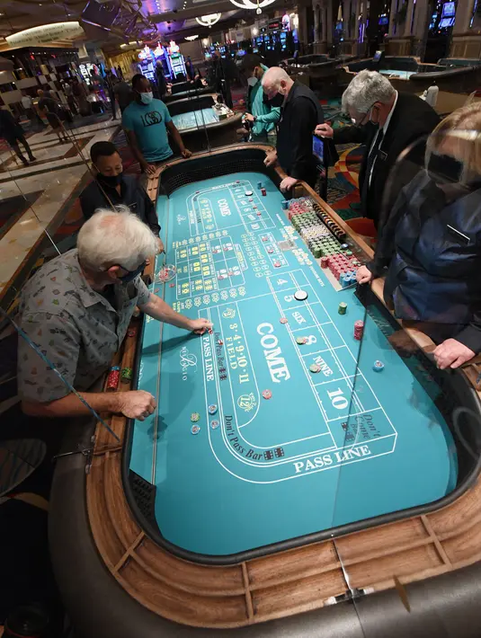 Para pengunjung bermain dadu dengan perisai keselamatan plexiglass di hotel dan kasino Bellagio, Las Vegas, Nevada, Amerika Serikat, Kamis (4/6/2020). Kasino di Nevada diizinkan kembali beroperasi setelah penutupan sementara untuk mencegah penyebaran COVID-19. (Ethan Miller/Getty Images/AFP)