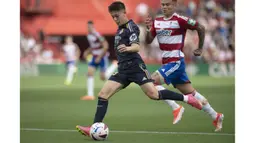 Pemain Real Madrid, Arda Guler (kiri) menggiring bola dibayangi pemain Granda, Kamil Piatkowski pada laga lanjutan Liga Spanyol 2023/2024 di Nuevo Los Carmenes Stadium, Granada, Sabtu (11/05/2024). (AFP/Jorge Guerrero)