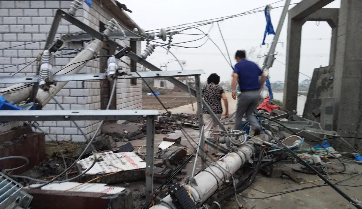 Warga berjalan diantara tiang lampu listrik yang berserakan di jalan akibat tornado yang menyapu wilayah Yancheng, Provinsi Jiangsu, Tiongkok, Kamis (23/6). Badai disertai hujan es telah menyebabkan kekacauan di Jiangsu. (STR/AFP)