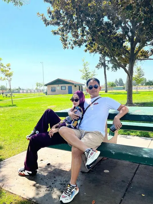 <p>Berpose bareng sang suami di sebuah taman, Zaskia tampil stylish mengenakan kemeja penuh warna dipadukan loose pants dan hijab warna magenta. (Instagram/zaskiadyamecca).</p>
