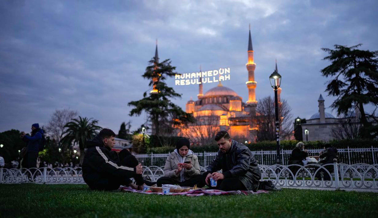 Orang-orang berbuka puasa selama bulan suci Ramadhan, di luar masjid Sultanahmet berlatar tulisan dalam bahasa Turki "Muhammad adalah utusan Allah", Istanbul, Turki, Rabu 25 Februari 2026. Sepanjang Ramadan, Masjid Sultanahmet di Istanbul, Turki, selalau ramai dikunjungi. (AP Photo/Emrah Gurel)